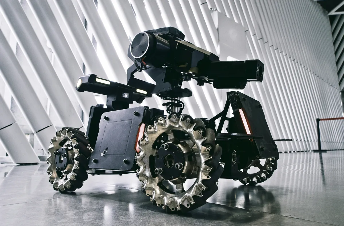 A wheeled inspection robot with an articulated sensor mast and rugged all-terrain wheels, photographed in an industrial facility.